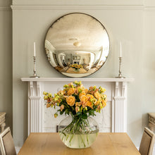 Load image into Gallery viewer, An aged silver round convex mirror on the mantlepiece of a traditional fireplace
