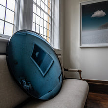 Load image into Gallery viewer, Aged Blue Round Convex Mirror placed on a cream linen sofa and reflecting a painting of clouds
