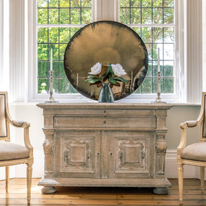 Aged Bronze Round Convex Mirror propped on a wooden sideboard in front of a bay window