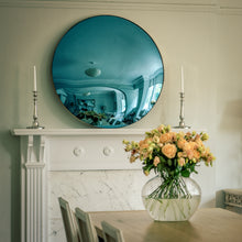 Load image into Gallery viewer, A Blue Round Convex Mirror placed on the mantelpiece of a traditional fireplace, and flanked by candles. A dining room table with a vase of yellow flowers is in the foreground.
