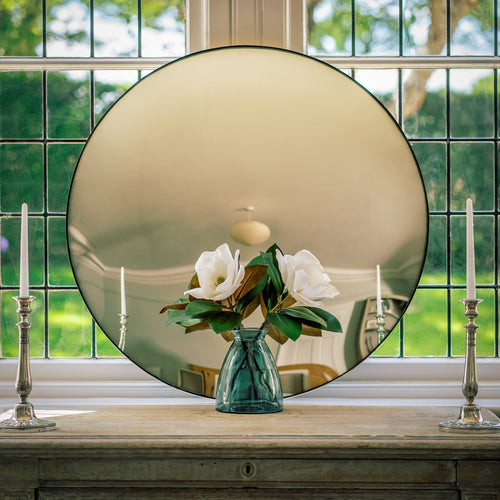 A Silver Round Convex Mirror propped on a sideboard which sites in front of a bay window